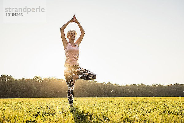 Ältere Frau macht Yoga auf einer ländlichen Wiese bei Sonnenuntergang