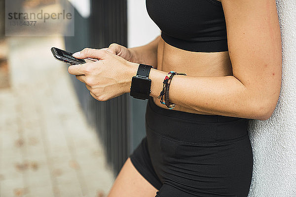 Passende junge Frau mit einer Smartwatch  die ein Smartphone benutzt