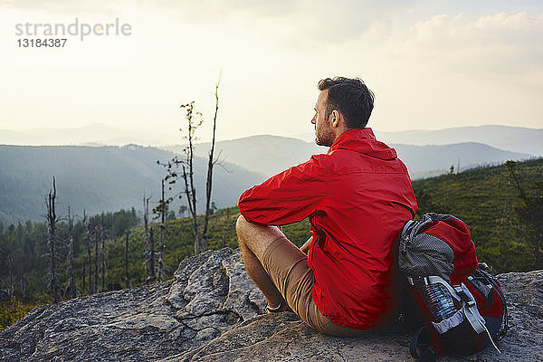Mann sitzt auf einem Felsen und genießt die Aussicht während einer Wanderung