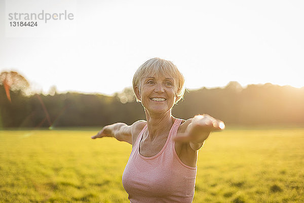 Porträt einer lächelnden älteren Frau beim Yoga auf einer ländlichen Wiese bei Sonnenuntergang