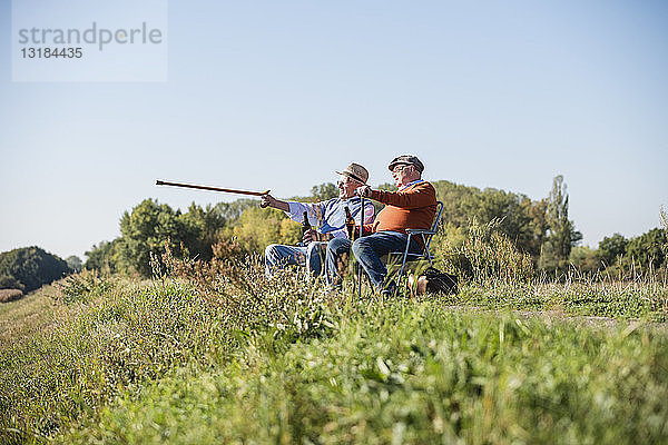 Zwei alte Freunde sitzen auf den Feldern  trinken Bier und zeigen mit einem Spazierstock auf sie