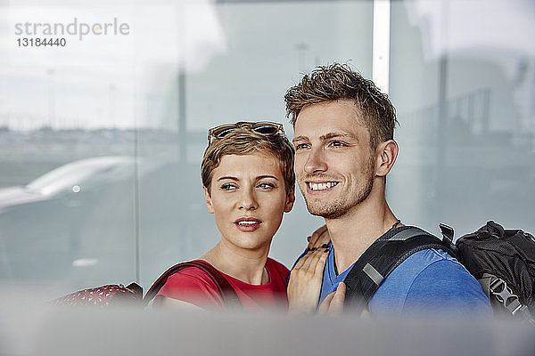 Porträt eines lächelnden Paares auf dem Flughafen  das aus dem Fenster schaut