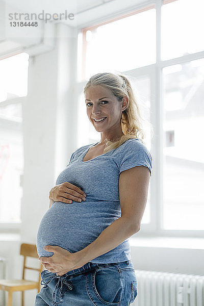 Porträt einer lächelnden schwangeren Frau am Fenster stehend