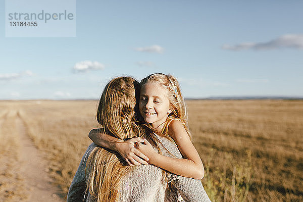 Lächelnde Tochter umarmt Mutter auf einem Feld