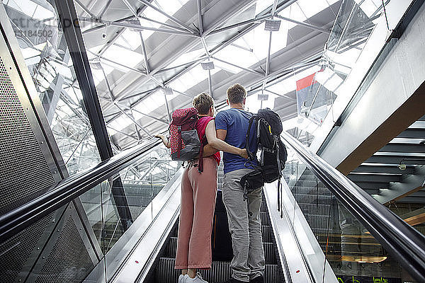 Rückansicht des Paares auf der Rolltreppe am Flughafen