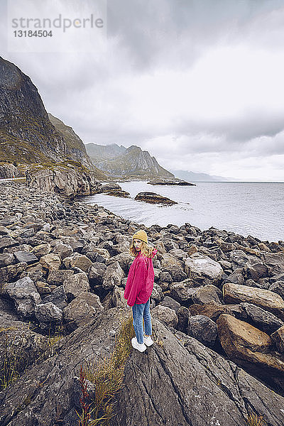 Norwegen  Lofoten  junge Frau in Regenjacke auf einem Felsen stehend