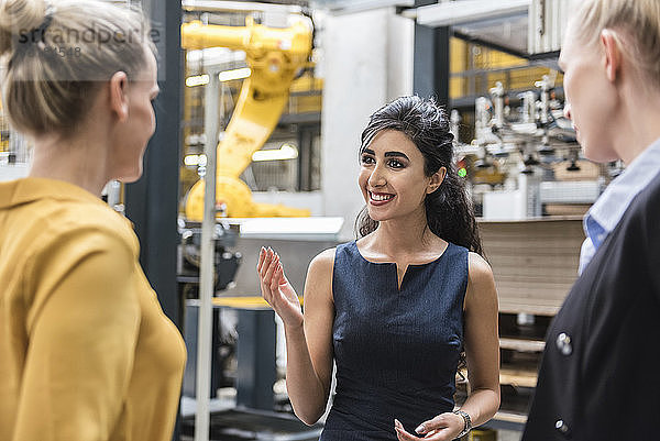 Porträt einer lächelnden Frau im Gespräch mit Kollegen in einer modernen Fabrik