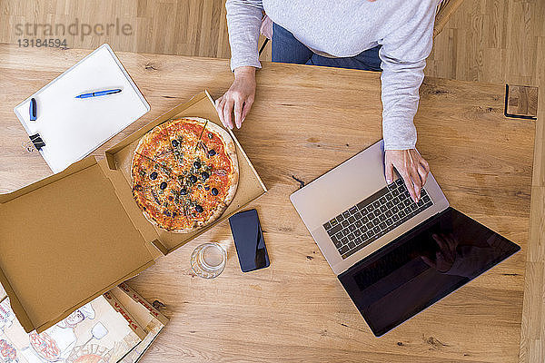 Frau im Home-Office mit Laptop beim Pizzaessen  Draufsicht