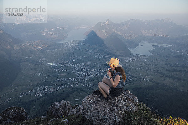 Schweiz  Grosse Mythen  junge Frau auf Wanderung  die bei Sonnenaufgang auf einem Felsen sitzt und aus einem Becher trinkt