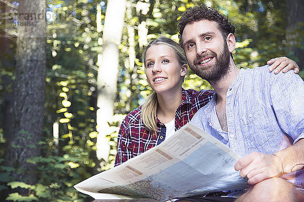 Lächelndes junges Paar mit Karte in einem Wald