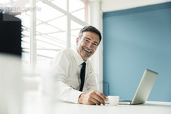 Porträt eines lachenden Geschäftsmannes mit Laptop auf einem Tisch im Büro