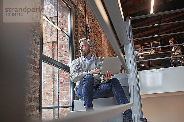 Geschäftsmann sitzt auf der Treppe eines modernen Büros und benutzt einen Laptop