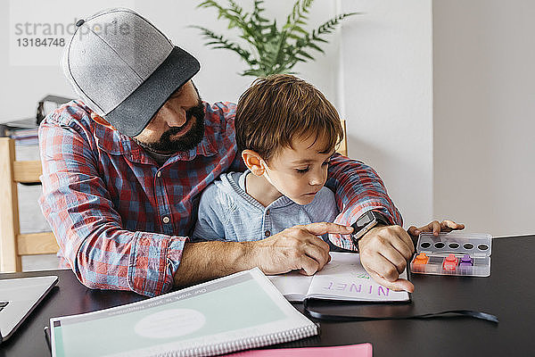 Vater erklärt seinem Sohn die Smartwatch  während er zu Hause arbeitet
