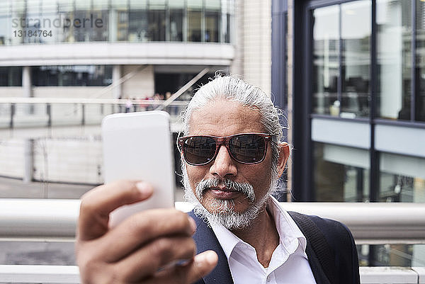 Porträt eines grauhaarigen Senior-Geschäftsmannes  der sich mit einem Smartphone selbstständig macht