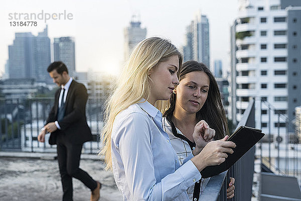 Zwei Geschäftsfrauen im Gespräch auf dem Dach der Stadt  mit einem digitalen Tablet