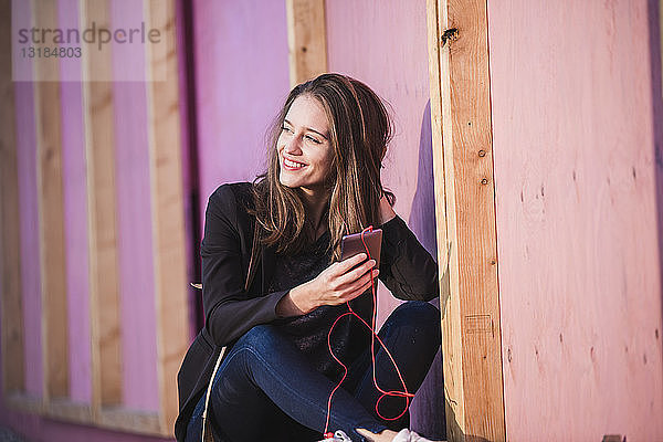Lächelnde junge Frau sitzt im Freien und hört Musik