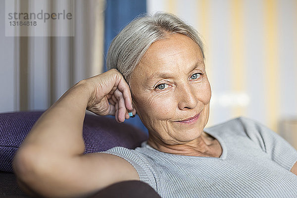 Porträt einer lächelnden älteren Frau  die sich zu Hause auf der Couch entspannt