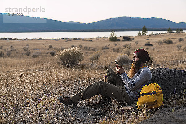 USA  Nordkalifornien  bärtiger junger Mann  der während einer Pause auf einer Wanderung in der Nähe des Lassen-Vulkan-Nationalparks sein Handy benutzt