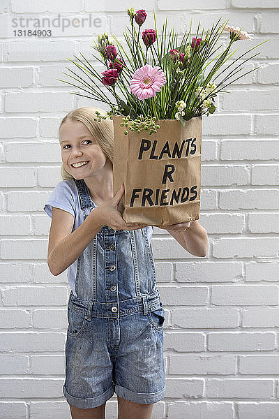 Porträt eines lächelnden Mädchens  das eine Papiertüte mit Blumen hält