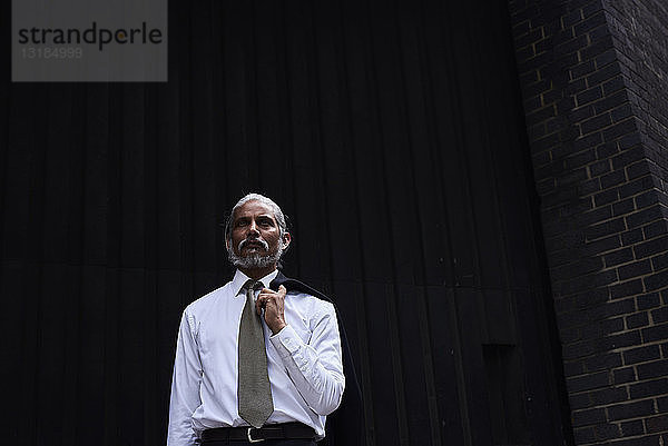 Porträt eines hochrangigen Geschäftsmannes mit grauen Haaren  weißem Hemd und Krawatte vor dunklem Hintergrund stehend