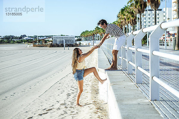 Mann hilft Frau beim Aufstieg vom Strand auf die Promenade