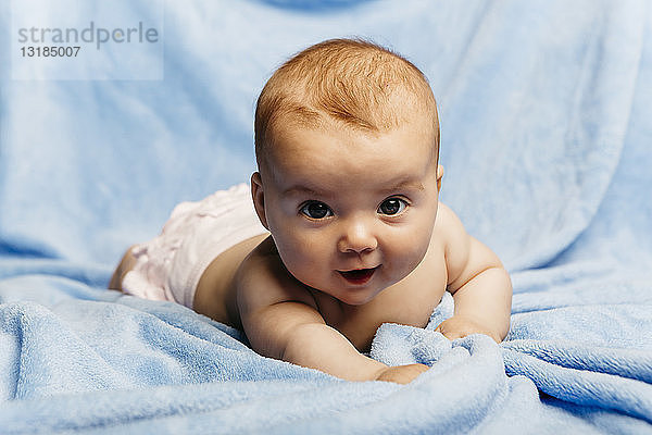 Bildnis eines lächelnden Mädchens auf einer hellblauen Decke liegend
