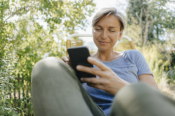 Frau sitzt im Garten auf Stuhl und benutzt Mobiltelefon