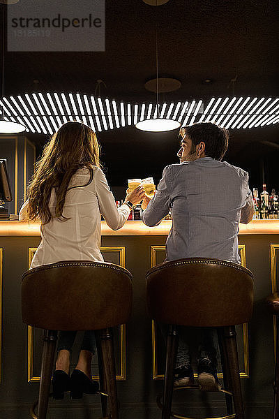 Rückansicht eines Paares  das in einer Bar an Biergläsern klimpert