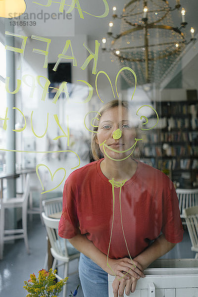 Porträt einer jungen Frau  die hinter einer Fensterscheibe in einem Cafe posiert