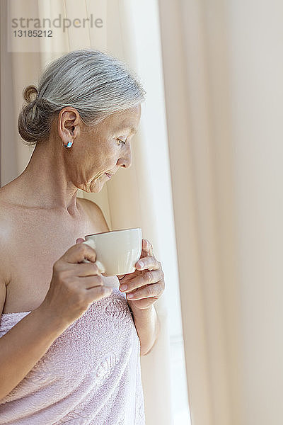 Ältere Frau in ein Handtuch gewickelt und trinkt morgens eine Tasse Kaffee