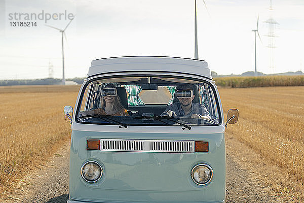 Lächelndes Paar mit VR-Brille fährt Wohnmobil in ländlicher Landschaft