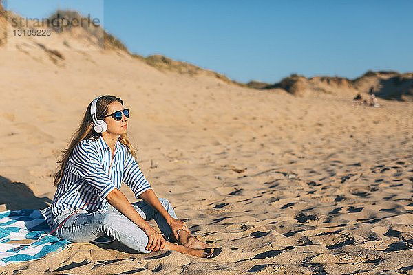 Portugal  Aveiro  Frau sitzt in der Nähe einer Stranddüne und hört Musik mit Kopfhörern
