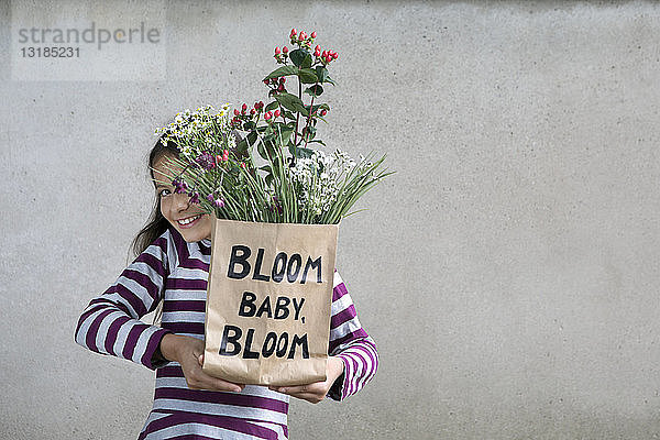 Lächelndes Mädchen hält Papiertüte mit Blumen