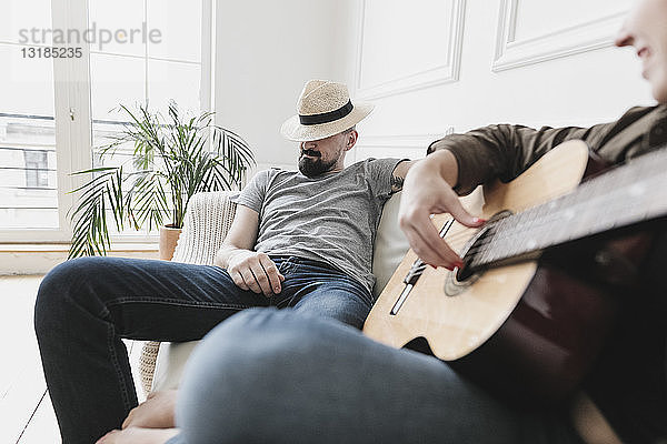 Entspanntes Paar sitzt auf Couch  Frau spielt zu Hause Gitarre