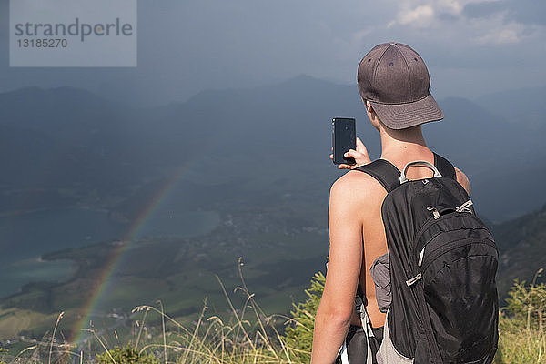 Österreich  Salzkammergut  Mondsee  Teenager beim Fotografieren eines Landschaftsbildes mit Regenbogen
