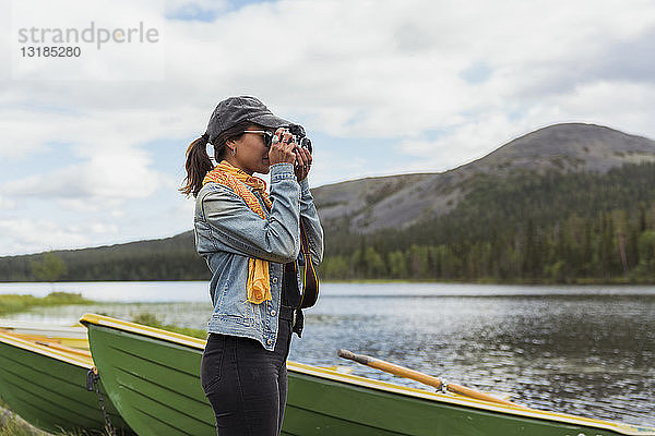 Finnland  Lappland  Frau beim Fotografieren mit einer Kamera am Seeufer
