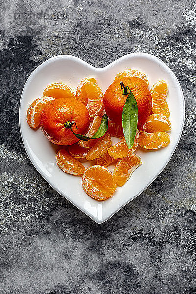Mandarinen mit Blättern  Stücke auf herzförmigem Teller