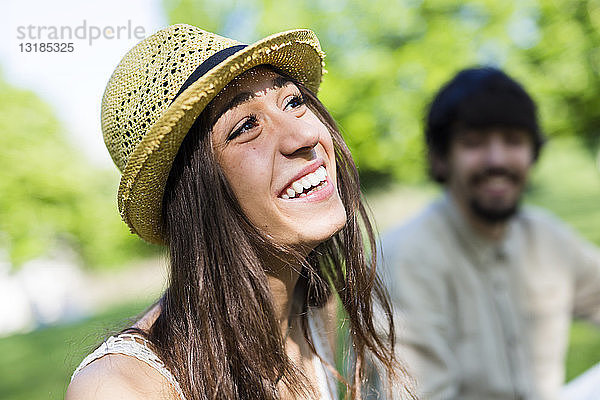 Porträt einer glücklichen jungen Frau in einem Park mit ihrem Freund im Hintergrund