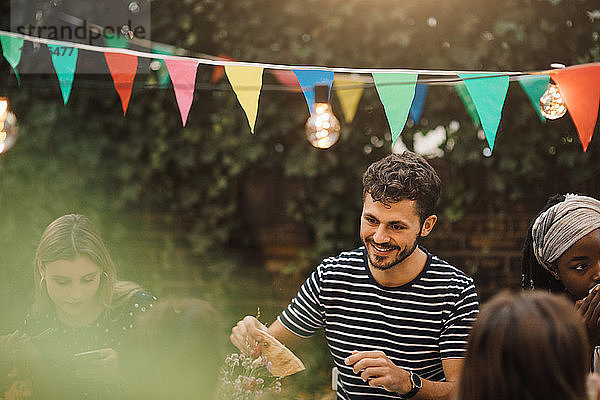 Lächelnder junger Mann genießt Dinnerparty mit Freunden im Hinterhof