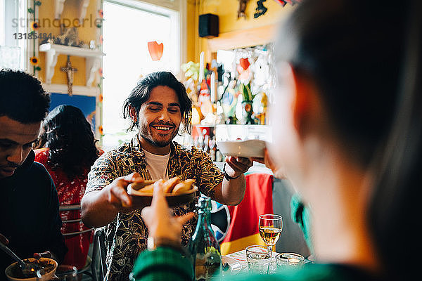 Lächelnder junger Mann gibt der Frau Essen  während er während der Brunch-Party bei einem Freund am Tisch im Restaurant sitzt