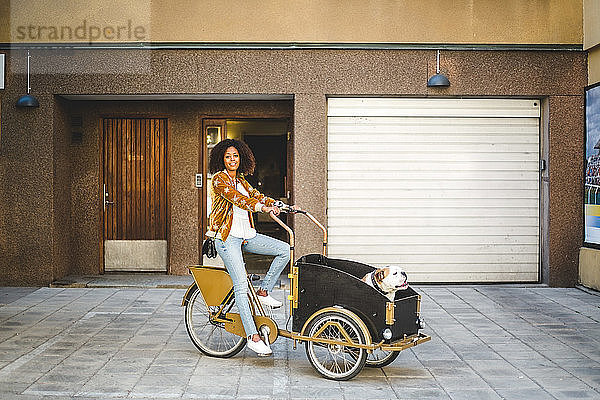 Mittlere erwachsene Frau in voller Länge auf Fahrradwagen mit Hund gegen Gebäude