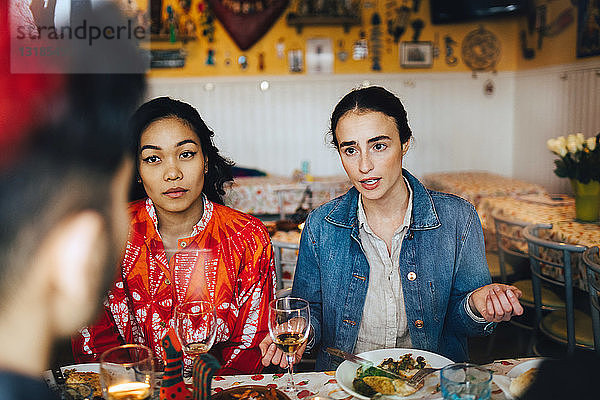 Junge Frauen im Gespräch mit einem männlichen Freund während einer Dinnerparty im Restaurant