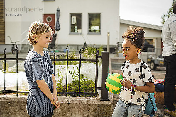 Lächelndes Mädchen hält Ball  während es mit Schwester gegen Haus spricht
