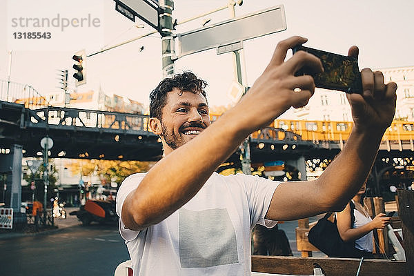 Lächelnder junger Mann fotografiert durch ein Smartphone  während er in der Stadt auf der Straße steht