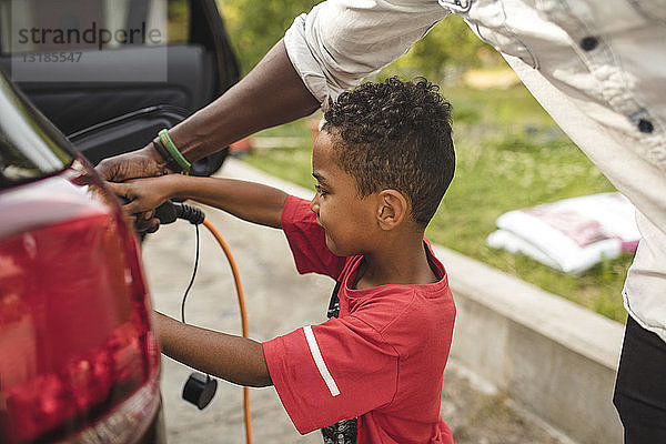 Ein Mann hilft seinem Sohn beim Aufladen des Elektroautos auf der Einfahrt im Vorgarten