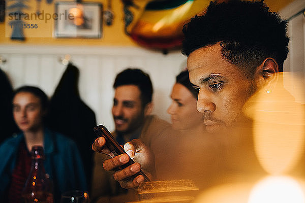 Junger Mann benutzt Smartphone  während er während einer Dinnerparty bei Freunden im Restaurant sitzt