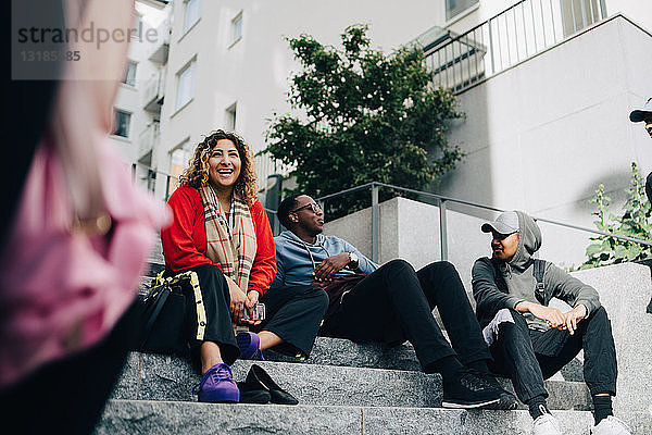Lächelnde männliche und weibliche Freunde sitzen auf Treppen in der Stadt