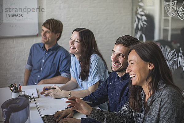 Kreative Geschäftsleute lächeln  während sie am Konferenztisch im Sitzungssaal sitzen