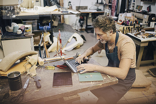 Männlicher Handwerker mit Laptop an der Werkbank in der Werkstatt