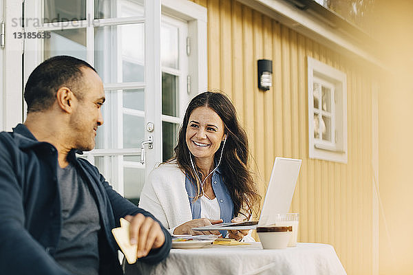 Lächelnde Frau zeigt Mann Laptop  während sie auf der Terrasse am Tisch sitzt